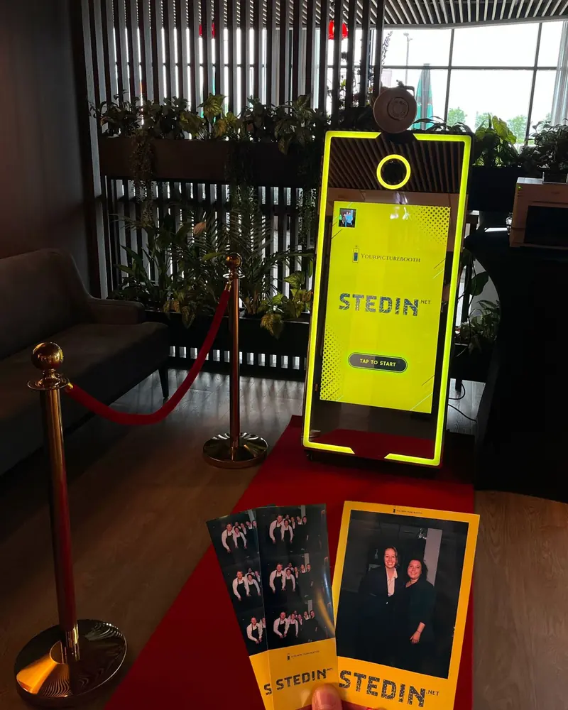 Spiegel photobooth in de gele huisstijl van Stedin, met geprinte fotostrips op de rode loper