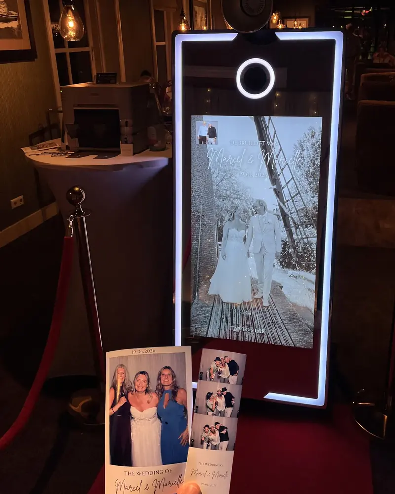 Spiegel photobooth met het startscherm van de bruiloft van Marcel en Mariëlle, met geprinte fotostrips op de voorgrond